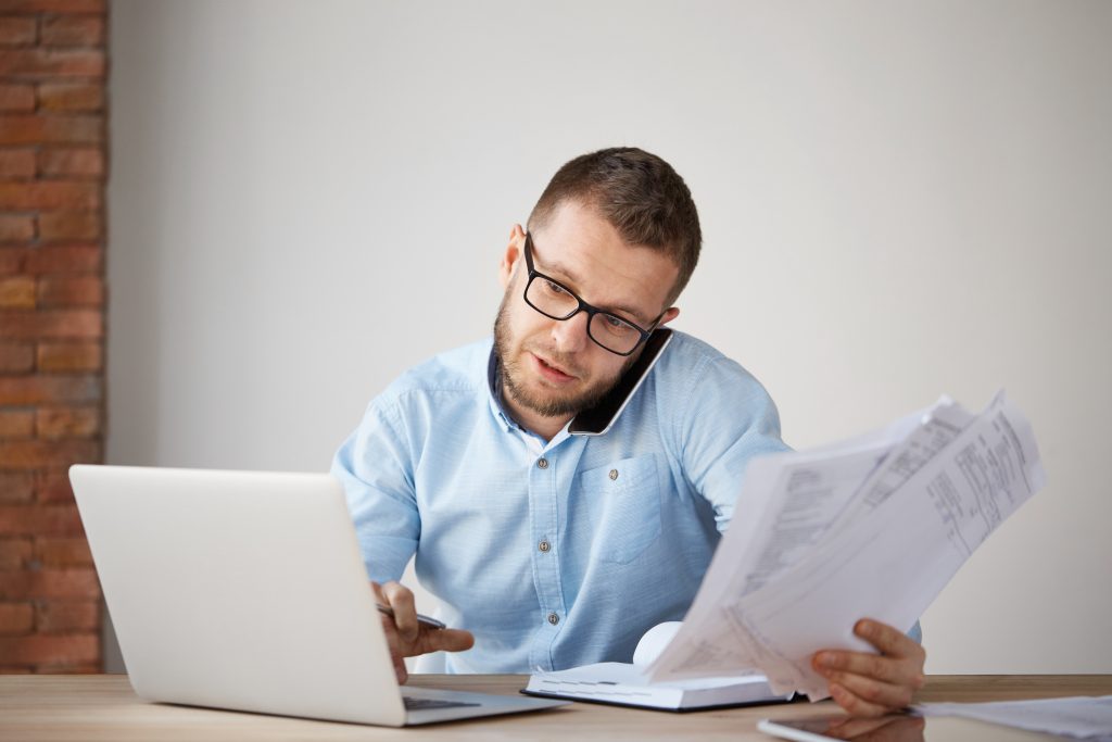 professional holding papers while using the phone and computer